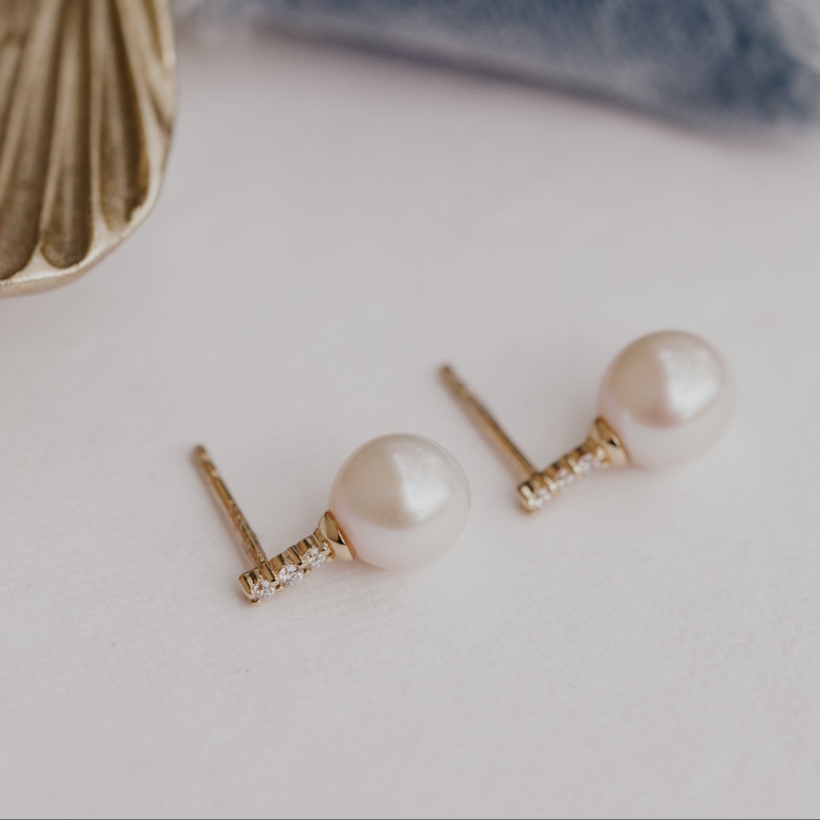 Pearl earrings with gold posts on a light background.