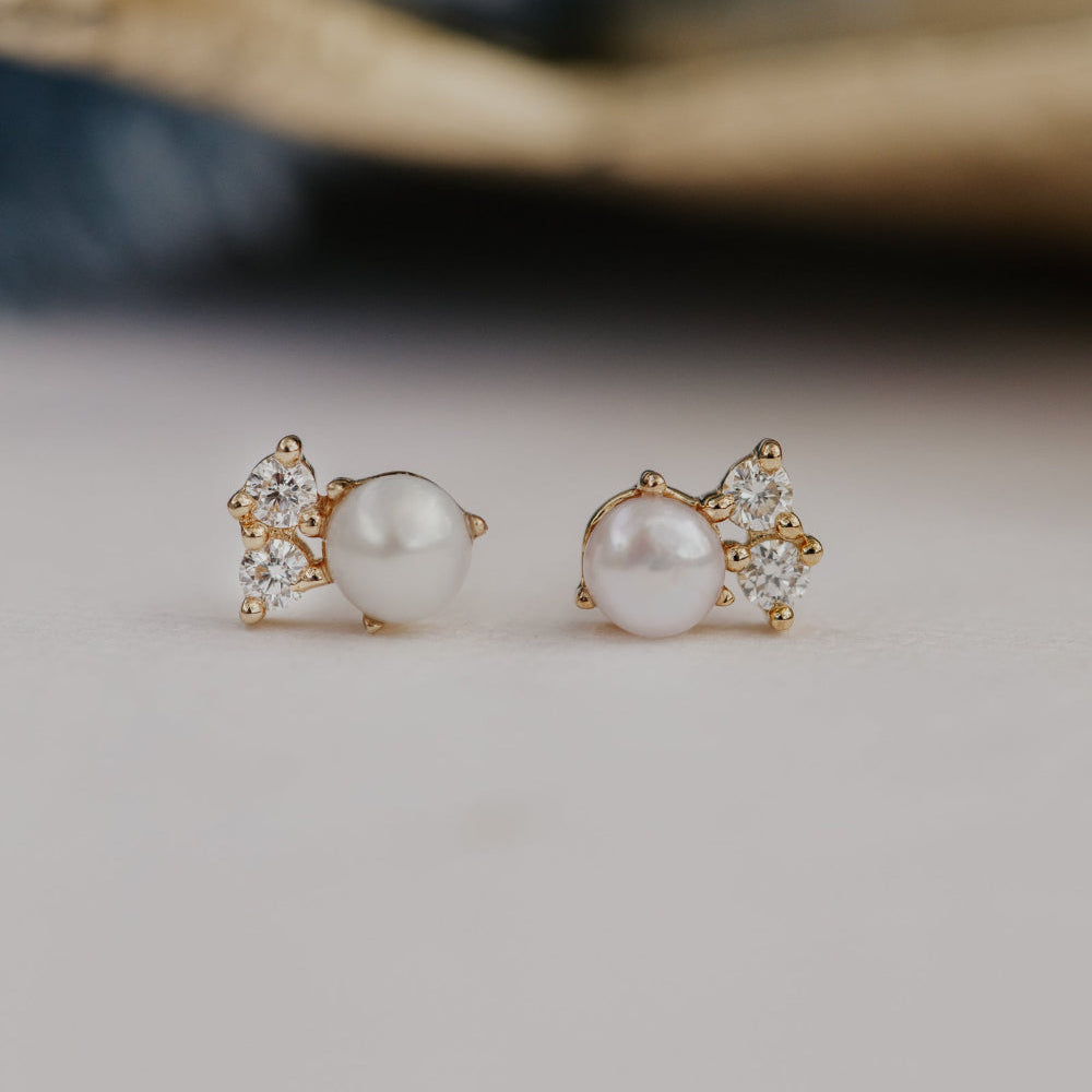 Pair of pearl earrings with gold and diamond accents on a neutral background.