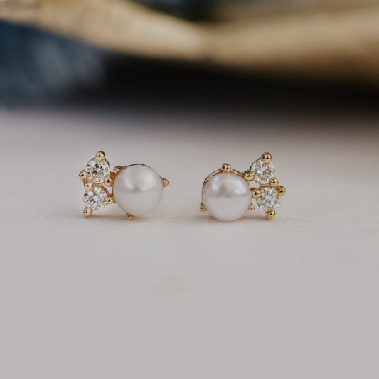 Pair of pearl earrings with gold and diamond accents on a neutral background.