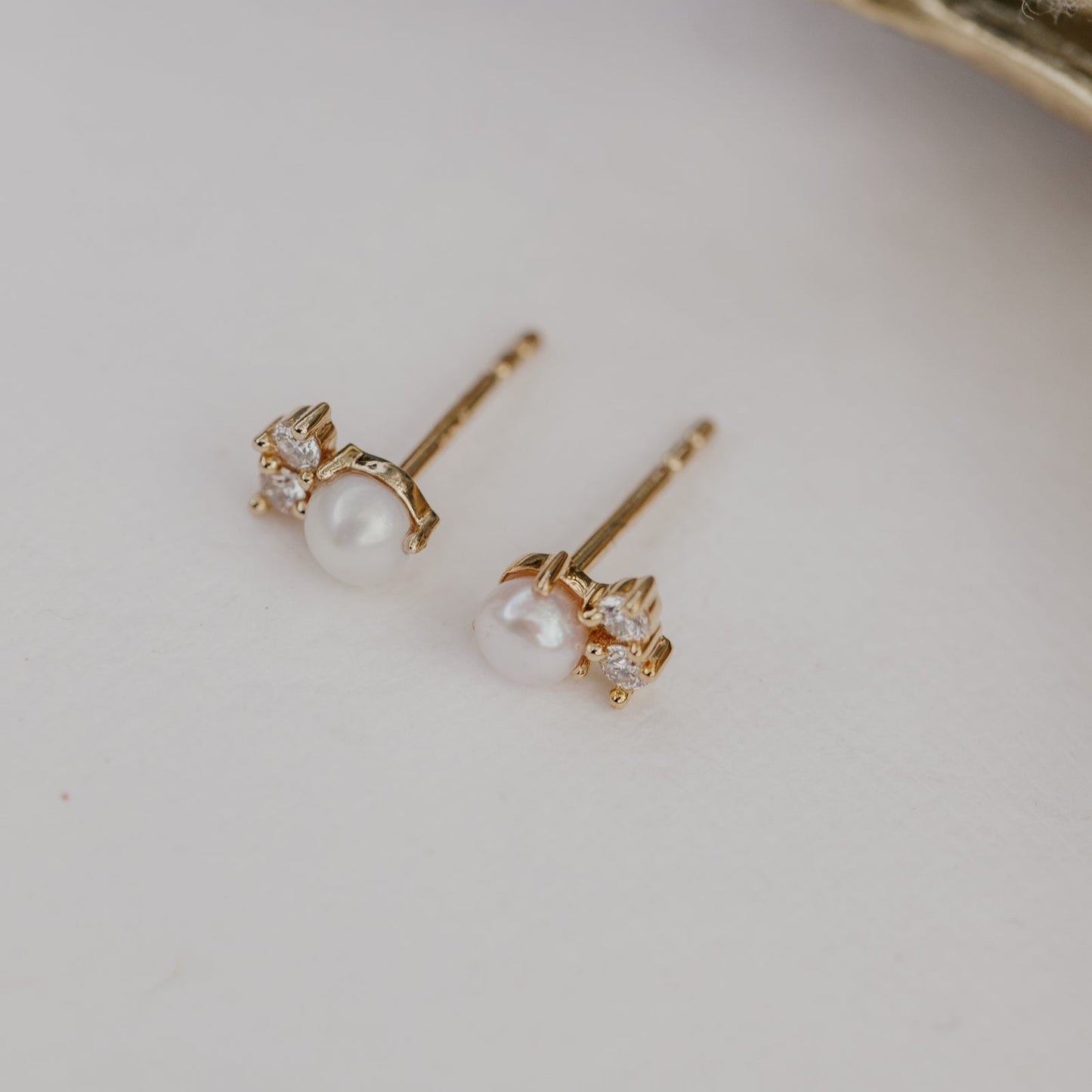 Gold earrings with pearls and small diamonds on a light background.