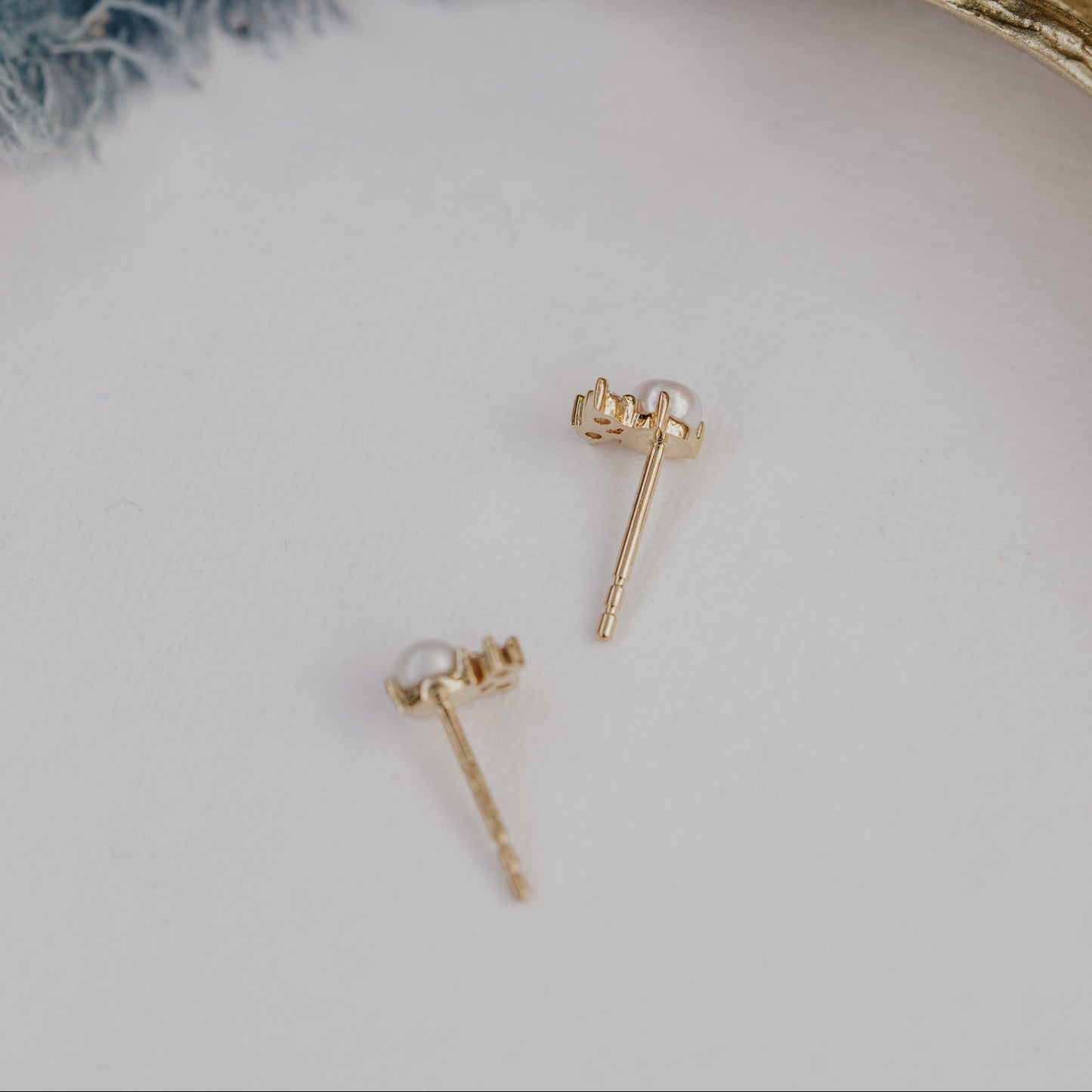 Gold earrings with pearls on a light gray background.