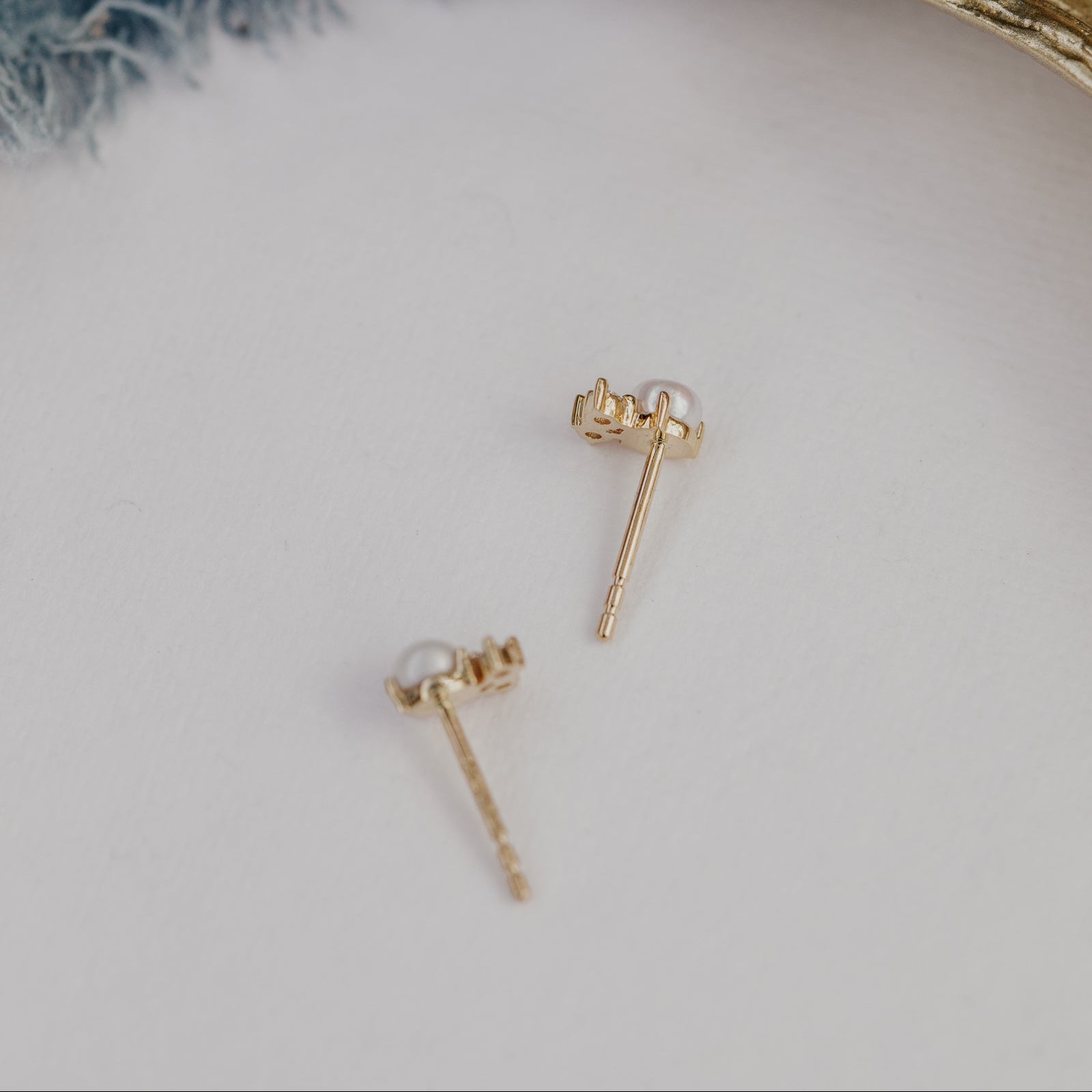 Gold earrings with pearls on a light gray background.