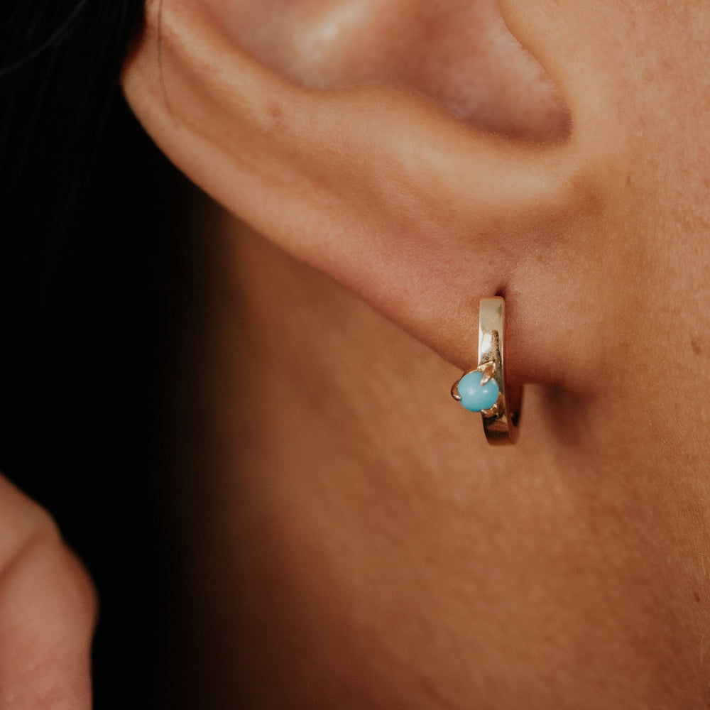 Close-up of an ear wearing a gold earring with a blue turquoise gemstone.