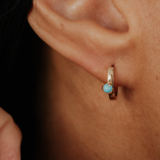 Close-up of an ear wearing a gold earring with a blue turquoise gemstone.
