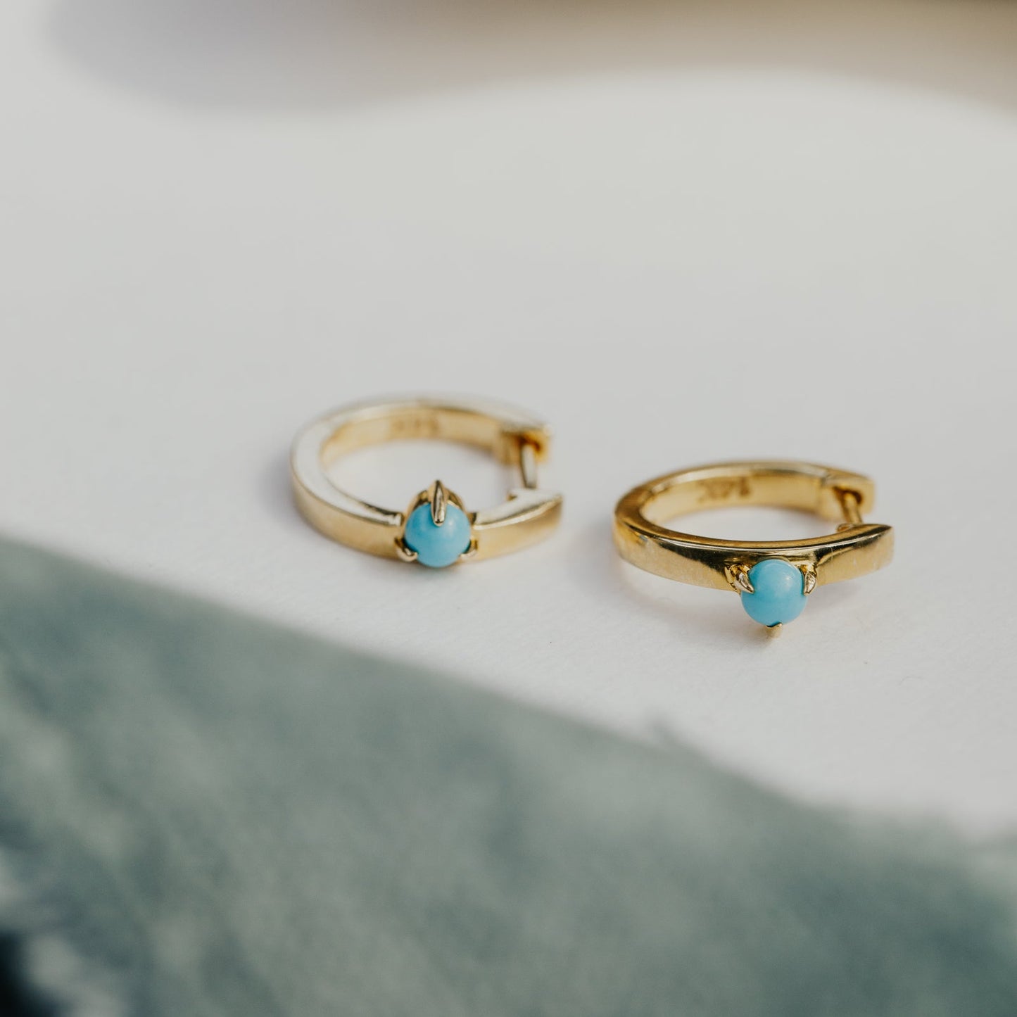 Gold hoop earrings with turquoise stones on a light background.