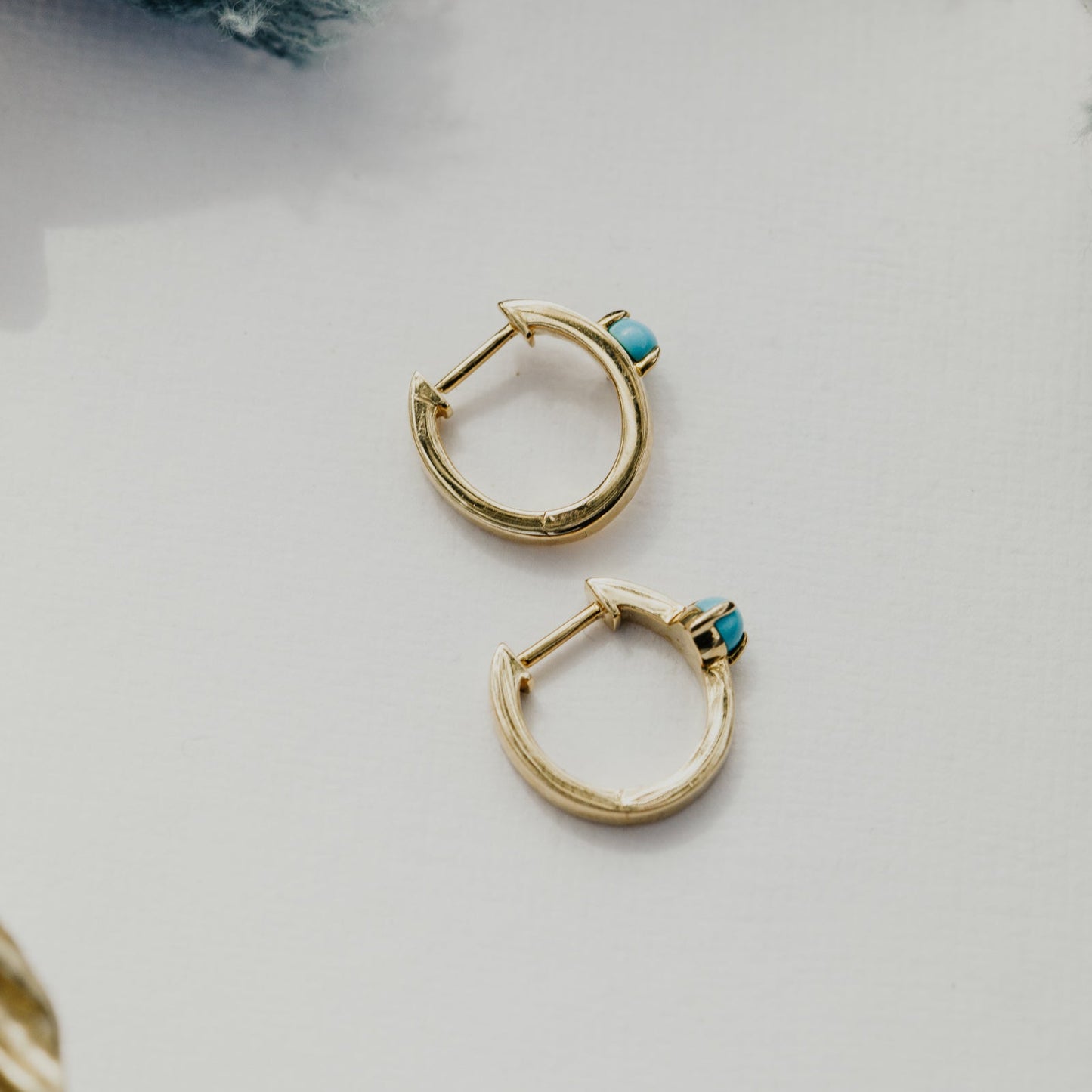 Gold hoop earrings with turquoise stones on a light background.