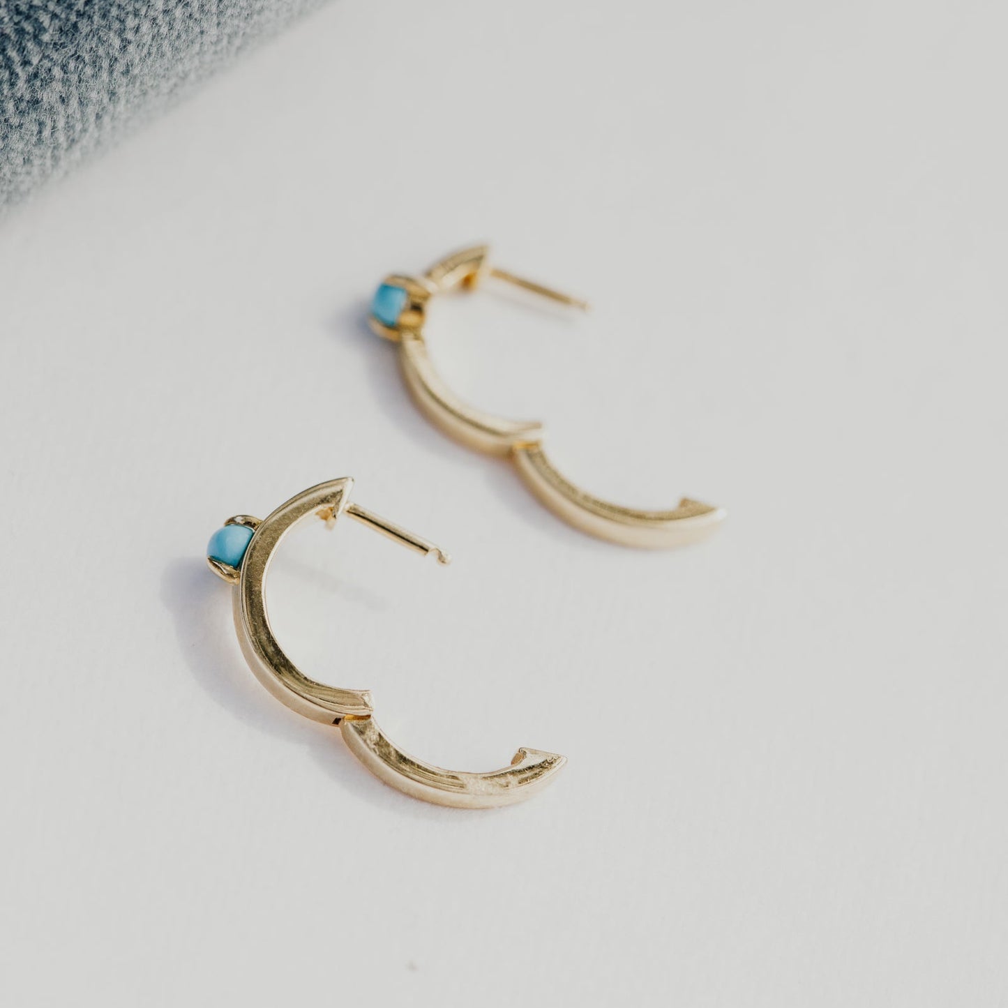 Gold hoop earrings with blue turquoise stones on a white surface.