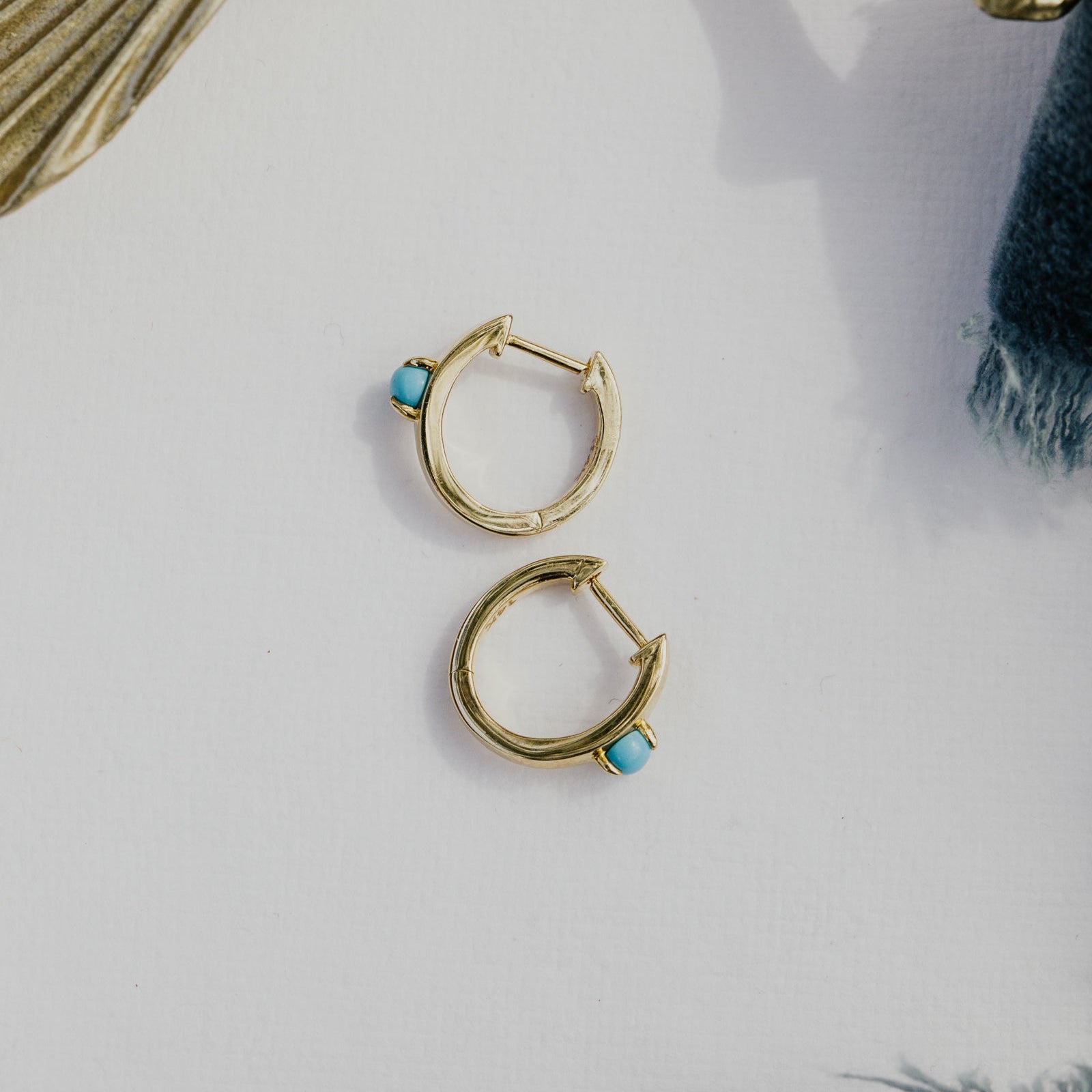 Gold hoop earrings with turquoise stones on a light surface with decorative elements.