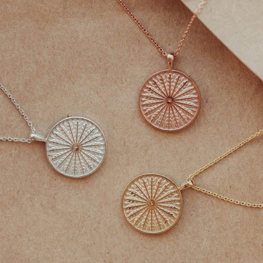 A gold necklace with a textured circular pendant in 14k yellow, white, and rose gold