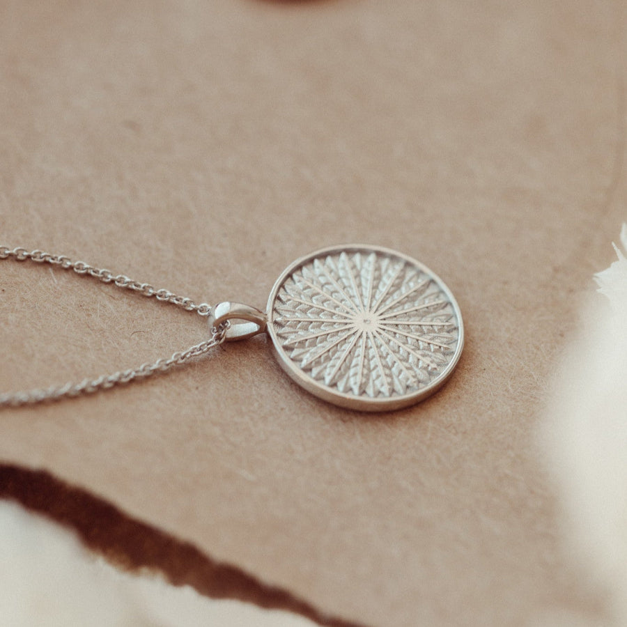 White gold necklace with a round, textured pendant on a soft beige background