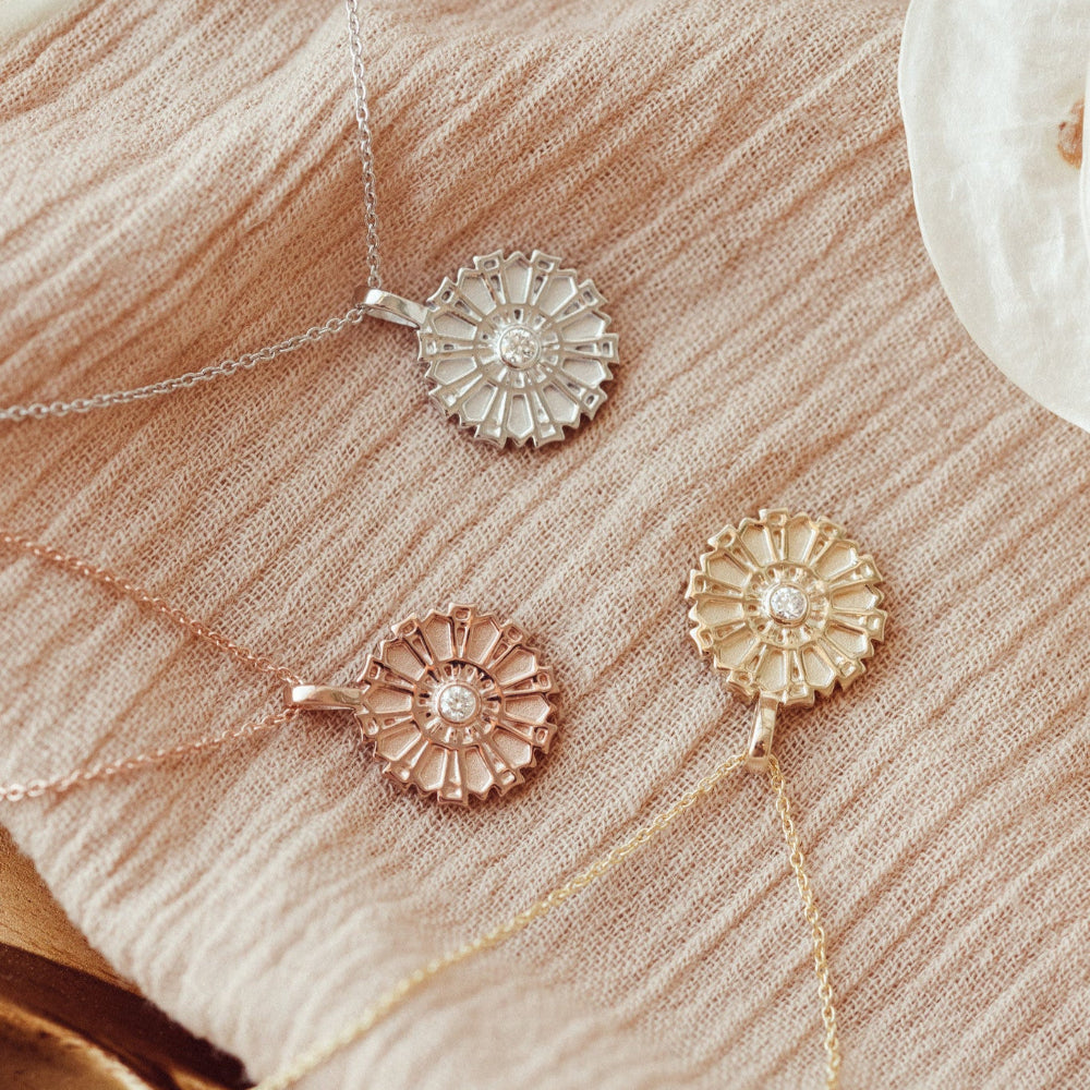 Three gold necklaces with floral pendants on a textured beige surface.