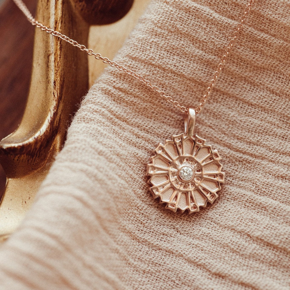 Rose gold sun-shaped pendant with a diamond on a beige fabric background