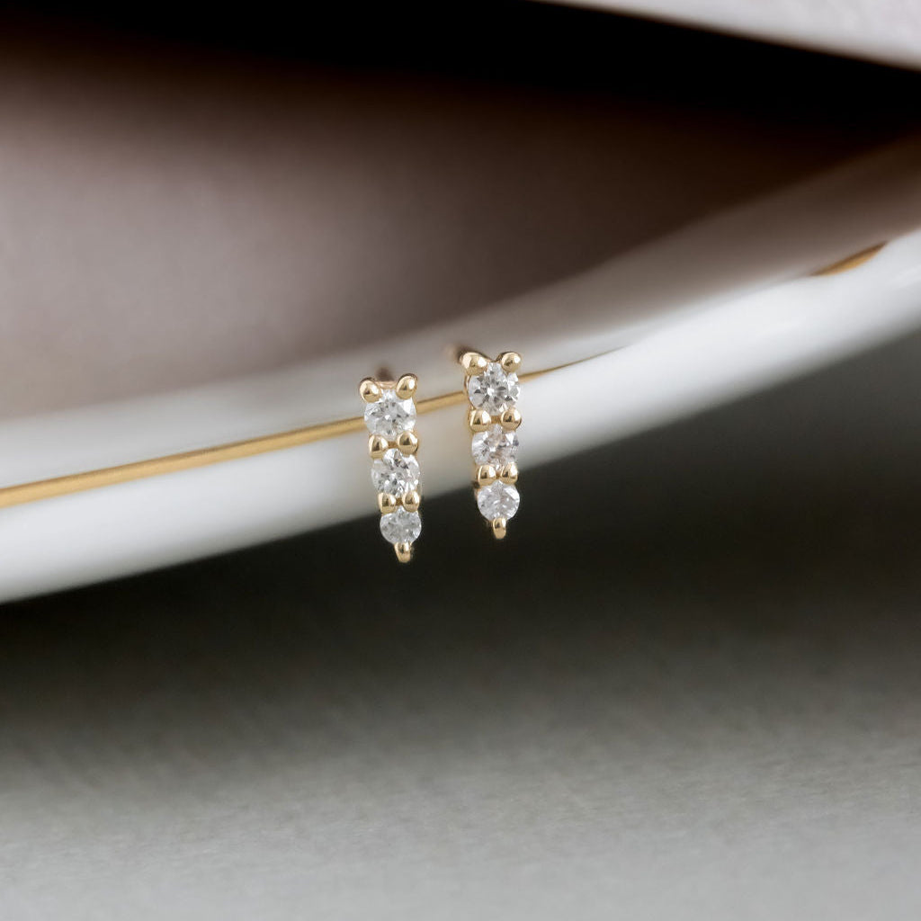 A pair of 14k yellow gold stud earrings with three tapered diamonds set in prongs, displayed on a white surface.