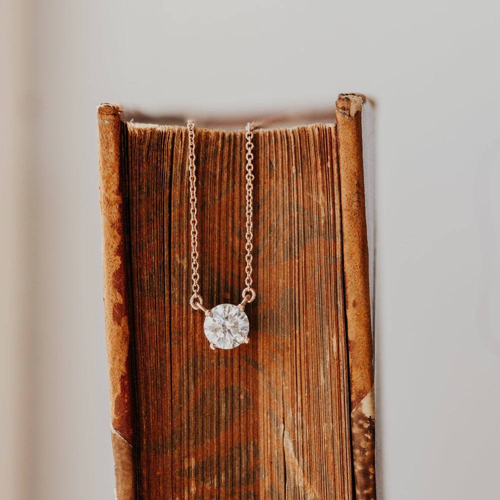 Necklace with a diamond pendant on an open book against a neutral background