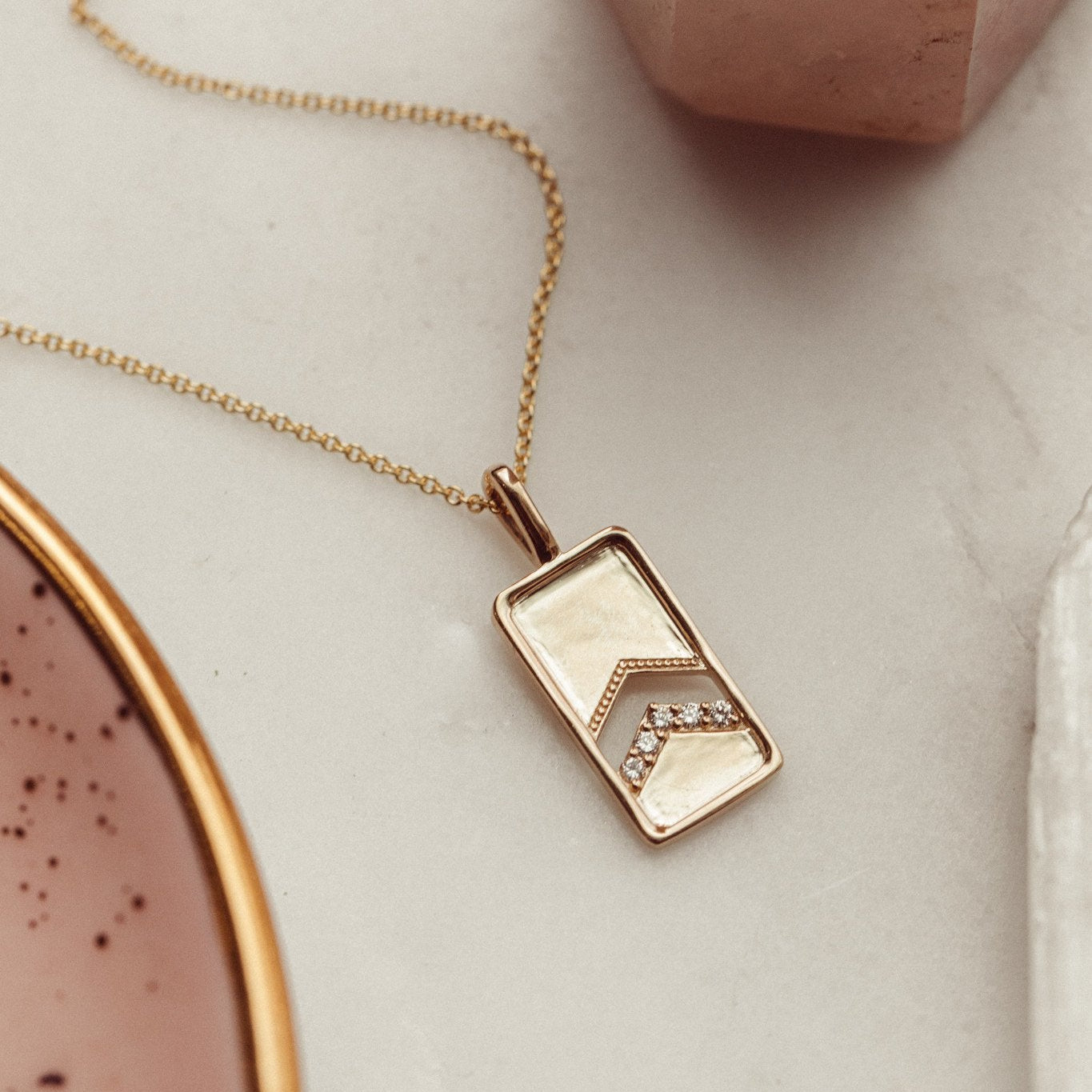 A 14k gold necklace with a rectangle pendant and round pave diamonds, displayed on a rolo chain.