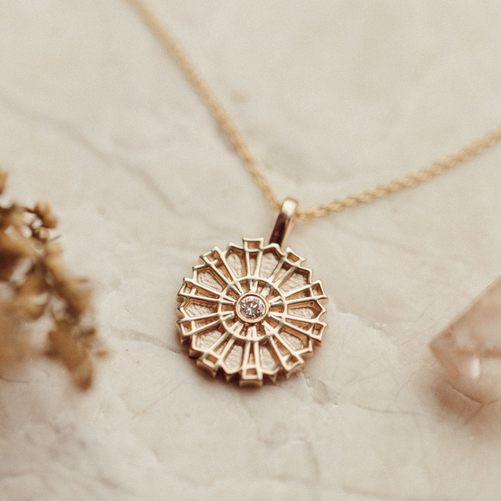 A 14k gold necklace with a medallion pendant and a small round diamond in the center, displayed on a rolo chain.