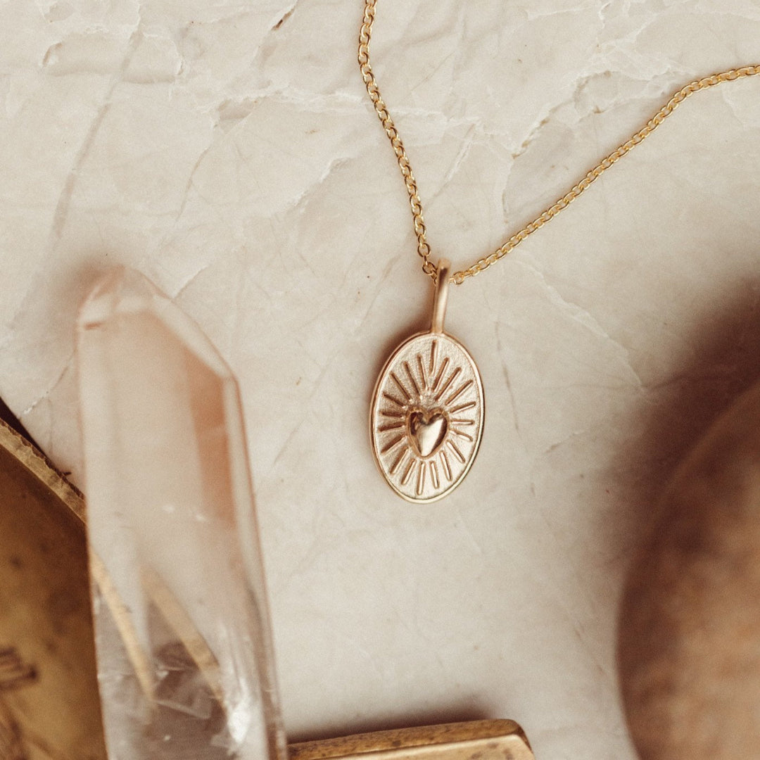 Gold necklace with a heart charm on a marble surface