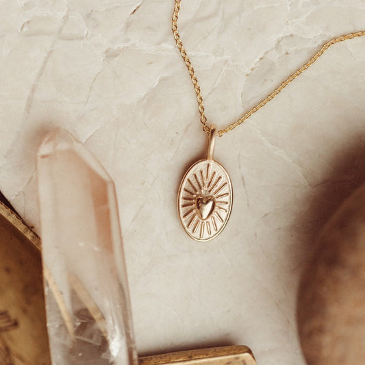 Gold necklace with a heart charm on a marble surface