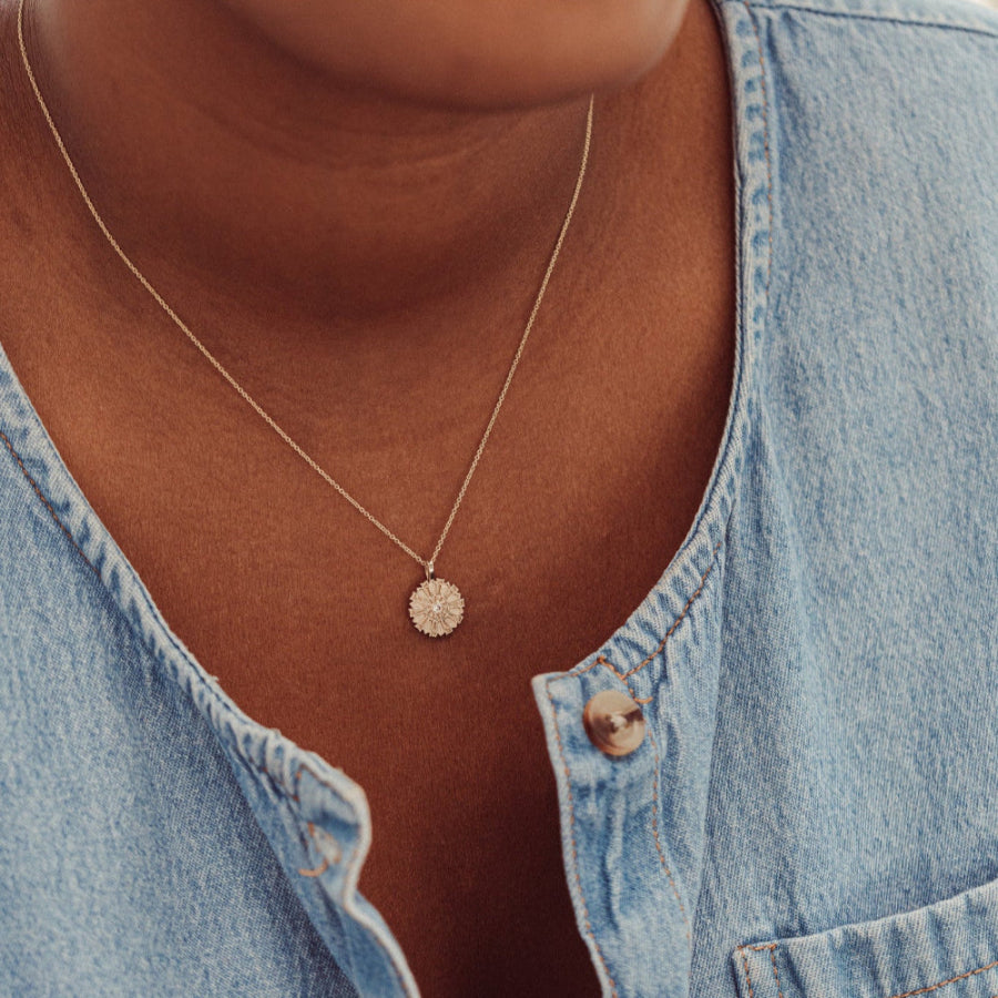 Person wearing a gold necklace with a small round pendant, close-up of the necklace.