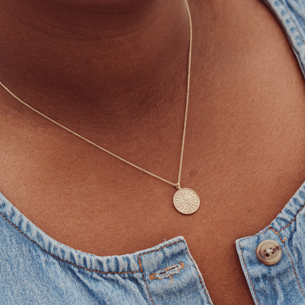 A gold necklace with a textured circular pendant, displayed on a models neck