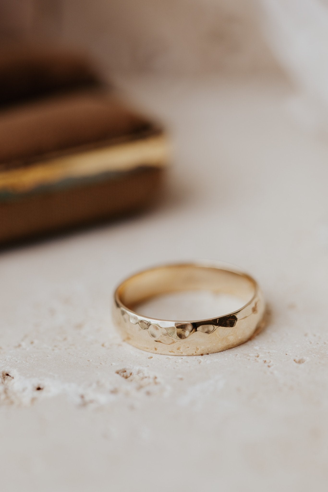 Close up of a hammered set gold Colbie band on a white textured surface.