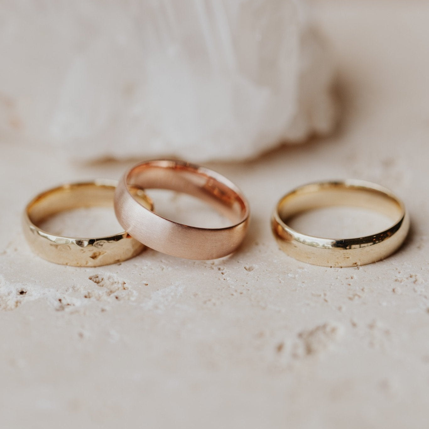 Three gold Colbie bands of different widths placed side by side on a textured surface.