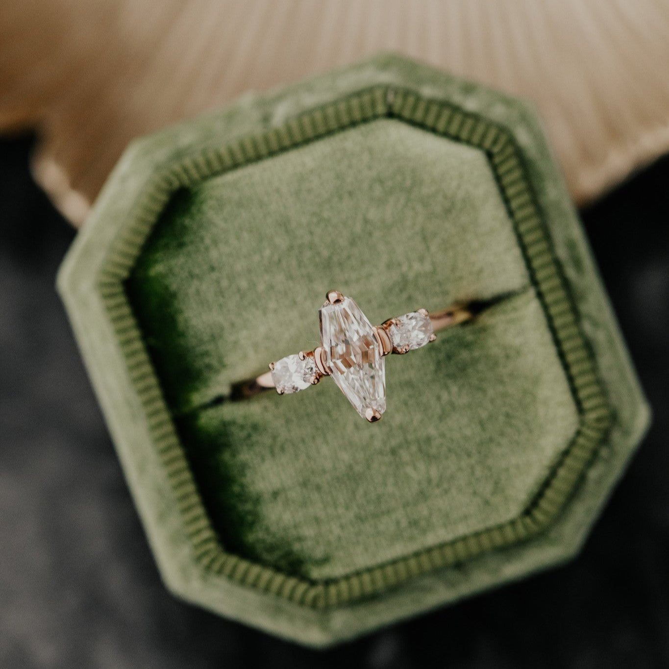 A modified kite shape diamond ring with side stones in a rose gold setting, presented in a green octagonal box.