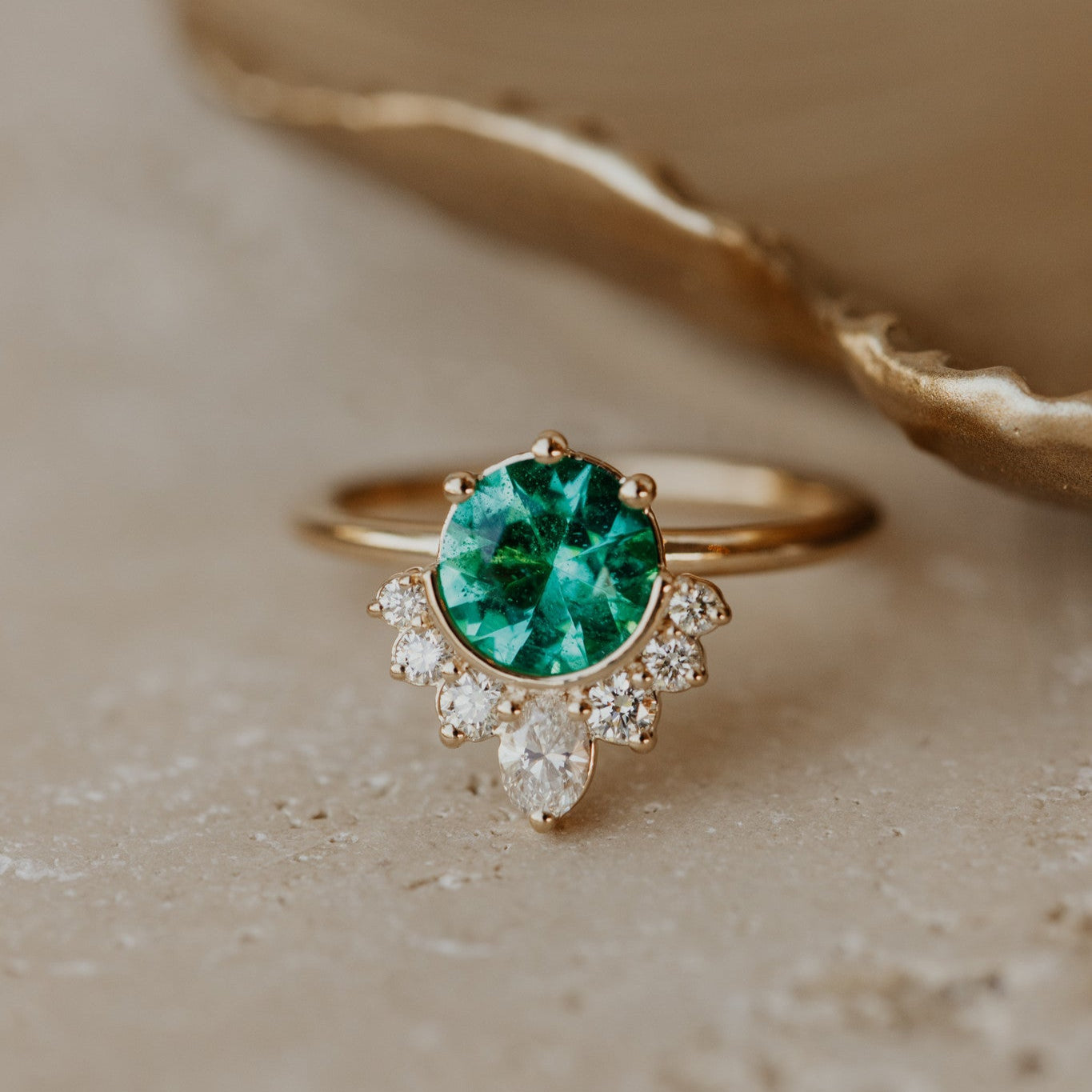 A 1.10 ct round bright green emerald ring with a half halo of oval and round diamonds set in a 14kyg band.