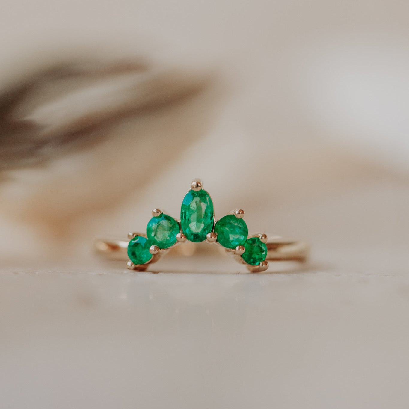 A gold band ring with multiple round and oval emeralds set in a starburst design, placed on a neutral background.