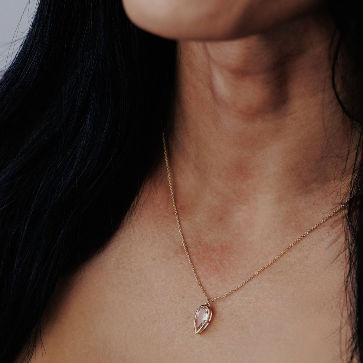 A 14k yello gold pear-shaped morganite necklace on the neck of a model. 