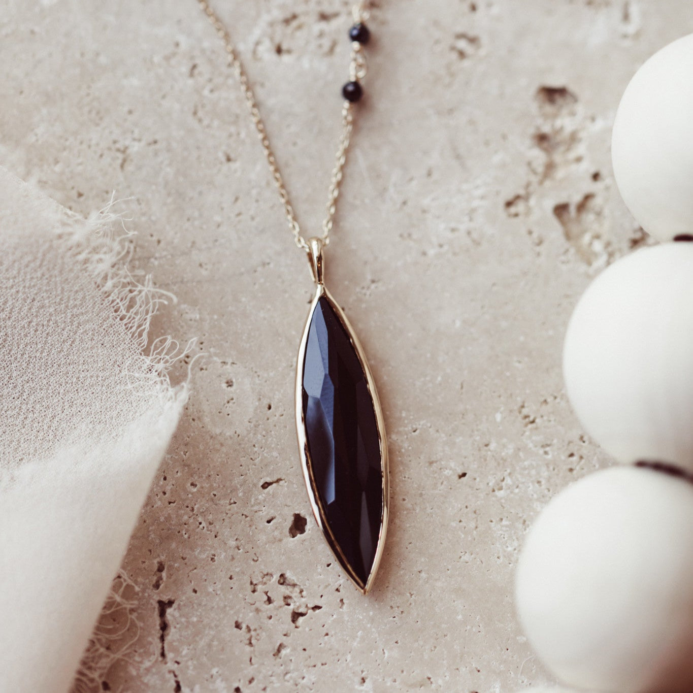 A 14k yellow gold necklace with a large marquise black spinel set in a high polished bezel, with three black spinel accents set on the chain, displayed against a neutral background.