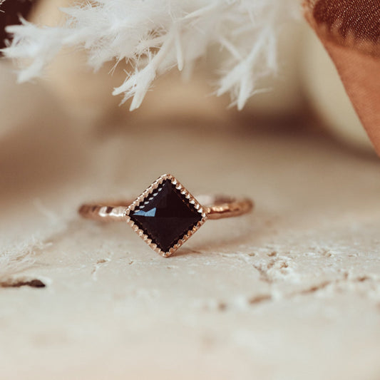 A square black spinel ring with a hammered textured band, set in a milgrain bezel, displayed against a neutral background.