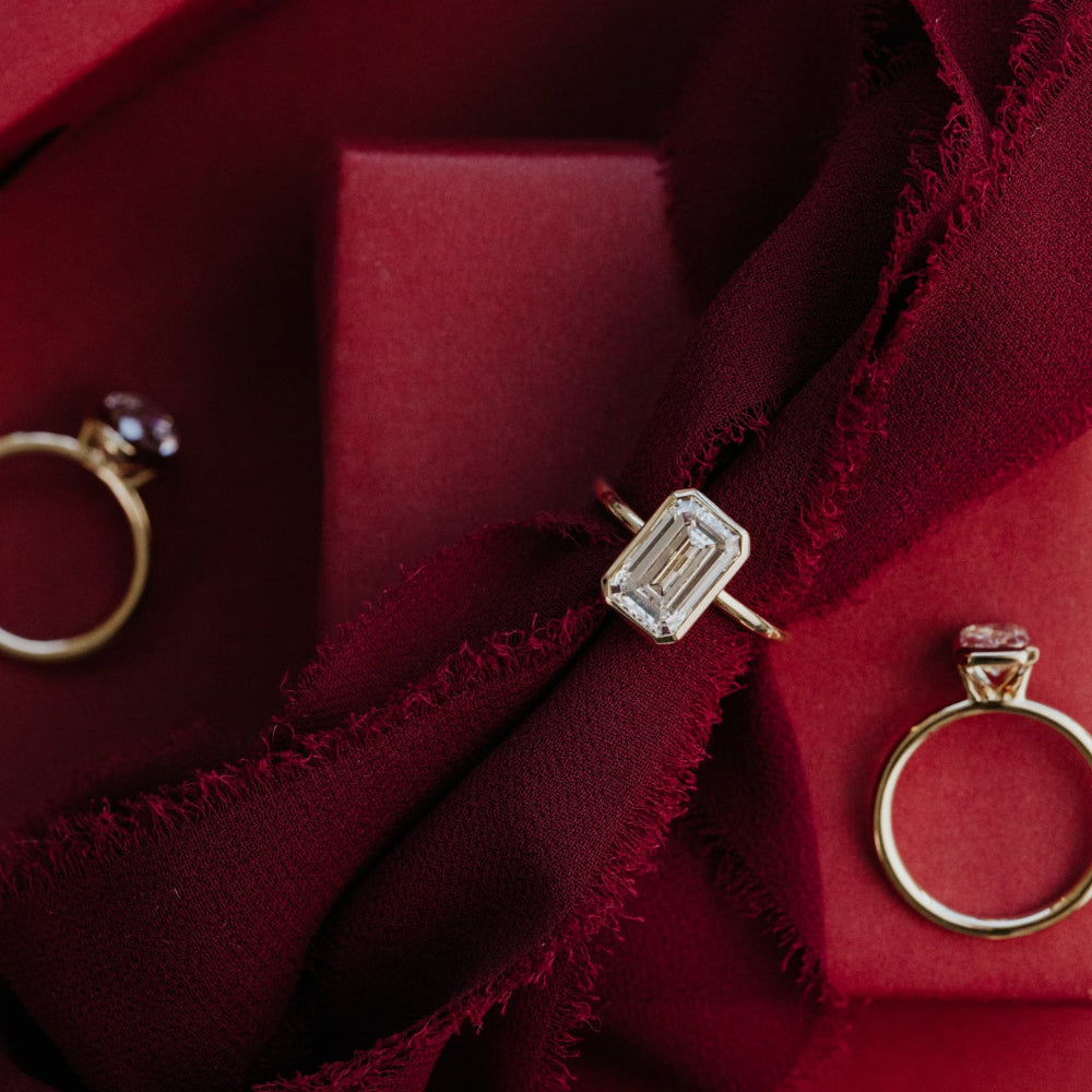 Gold rings with emerald cut on a red fabric background