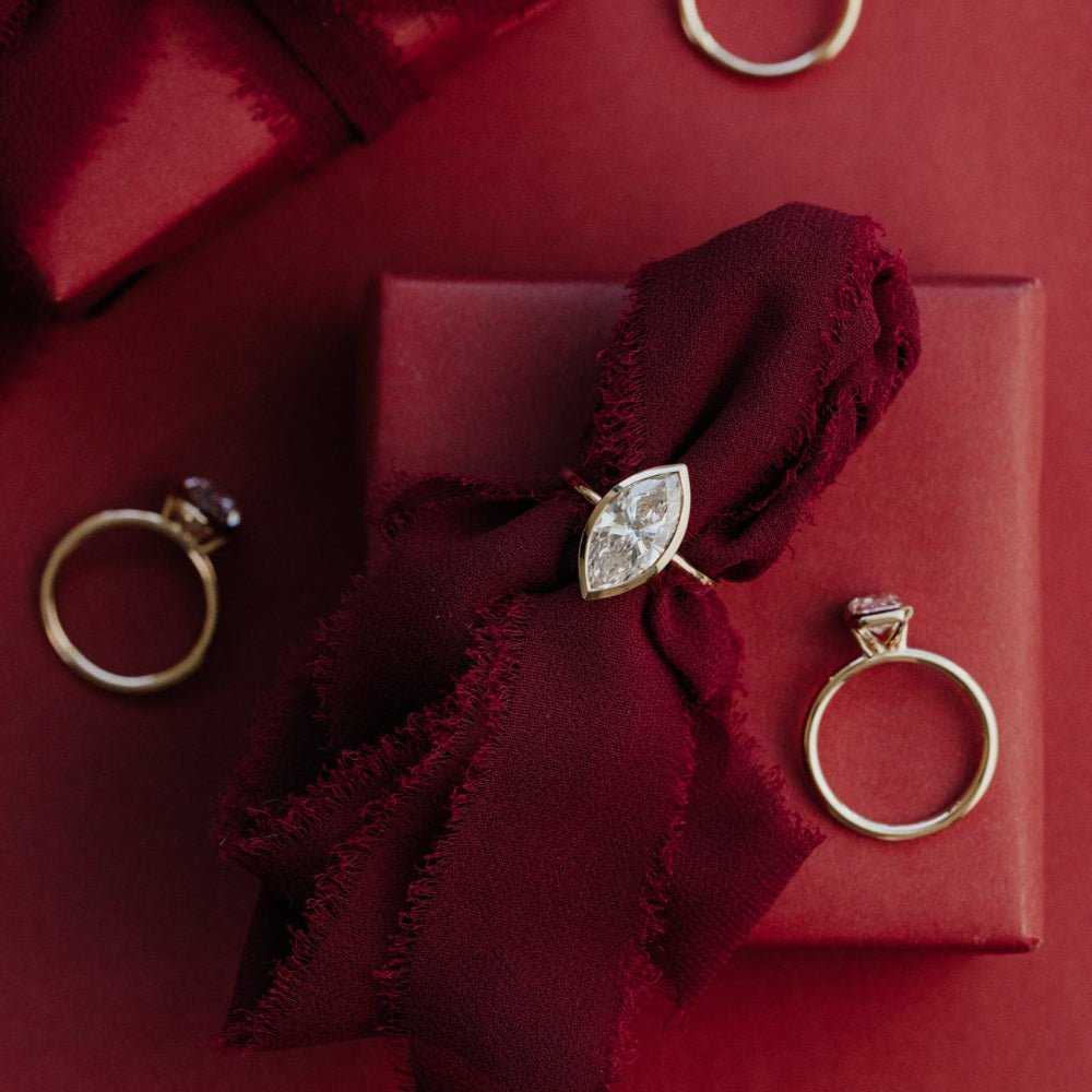 Gold marquise diamond rings on a red fabric with a red box in the background