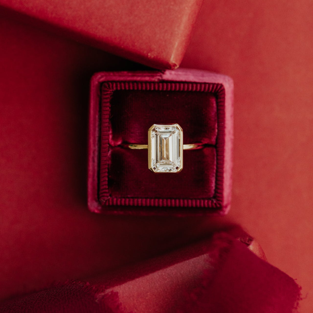 Gold ring with a emerald cut diamond in a red velvet box on a red background