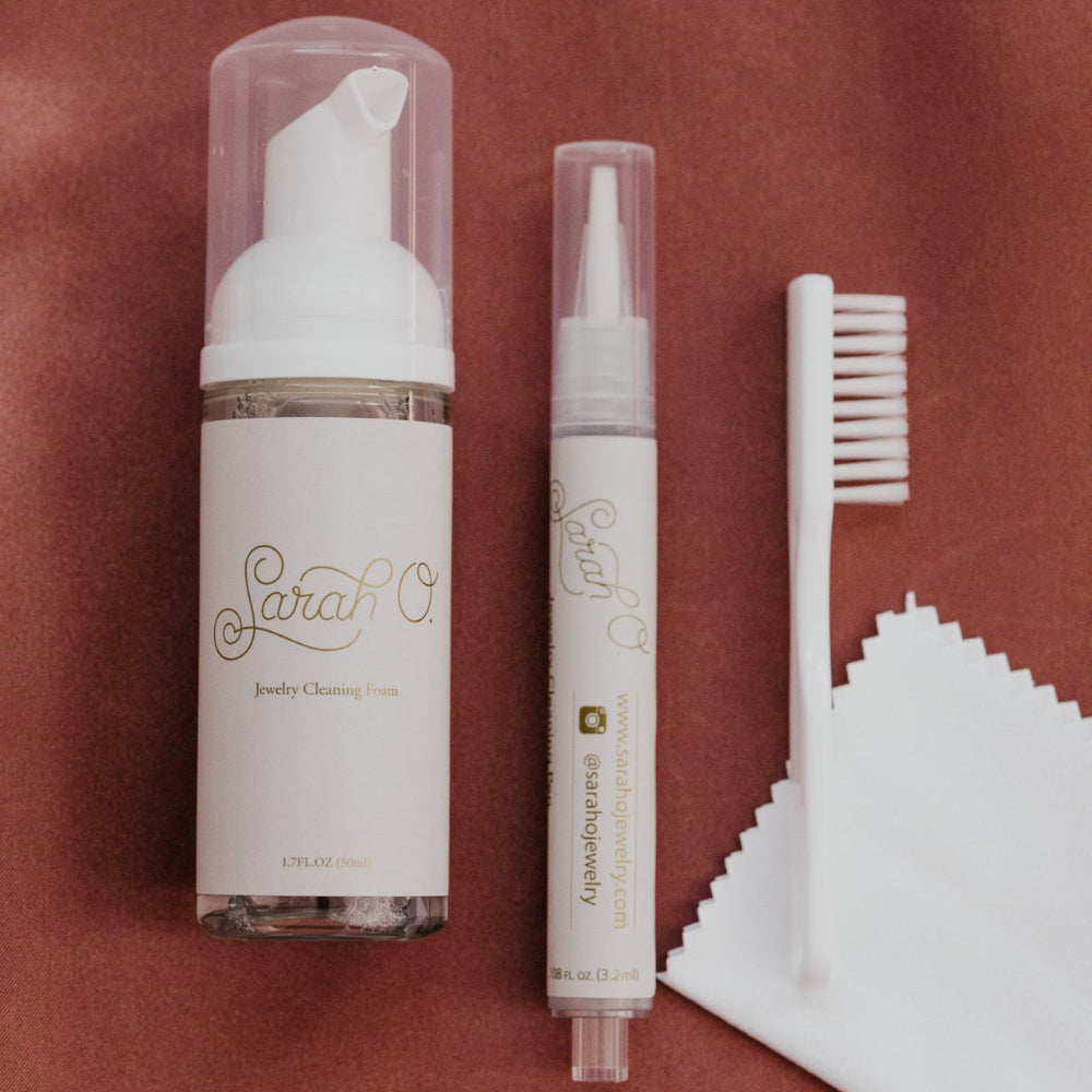 Jewelry cleaning products including a foam bottle, pen, brush, and cloth on a red background.