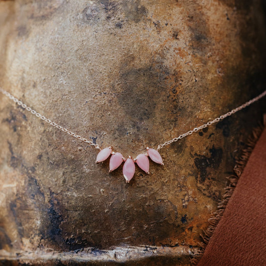 A curved necklace with pear and marquise shaped pink opals set in rose gold prongs, displayed on a textured surface.