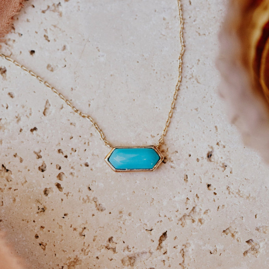 A long hexagon turquoise bezel necklace laid out on a textured surface.