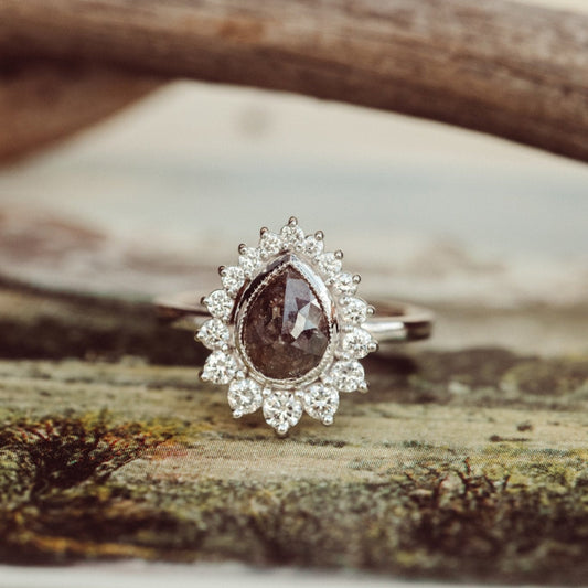 white gold ring with a large brown rustic diamond and smaller diamonds on a wooden surface
