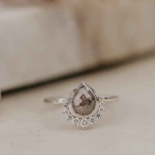 White Gold Acadia ring with a pear-shaped gray brown rustic diamond and diamond halo on a neutral background.