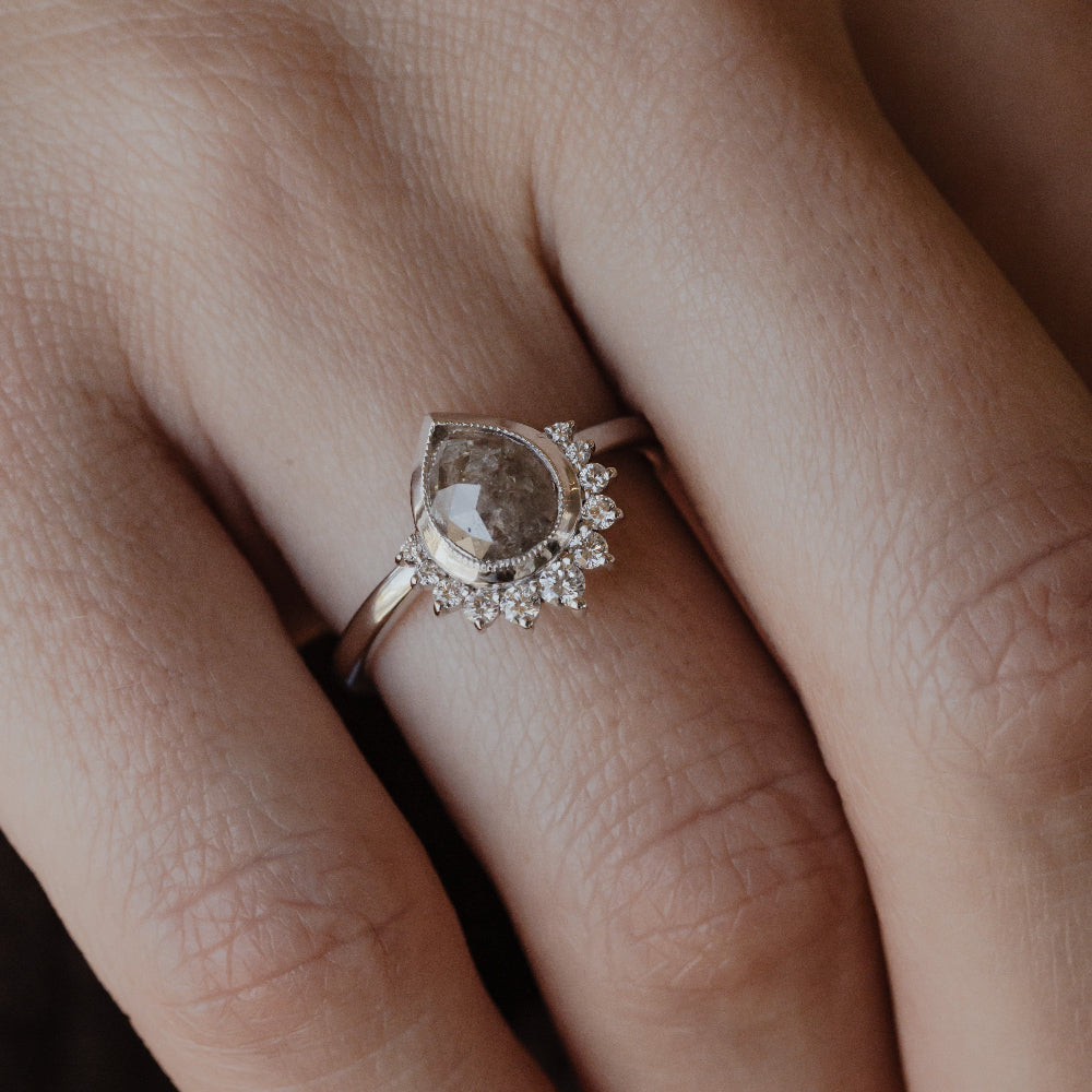 Close-up of a hand wearing a white gold pear shaped rustic diamond ring.