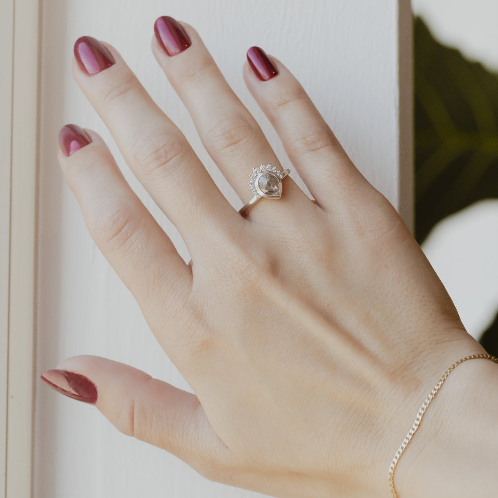 Hand with a pear rustic diamond ring on a neutral background