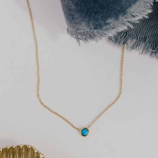 Gold necklace with a turquoise pendant on a light background.