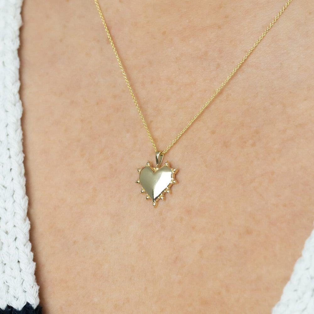 Gold heart-shaped pendant necklace on a person wearing a white and black outfit.