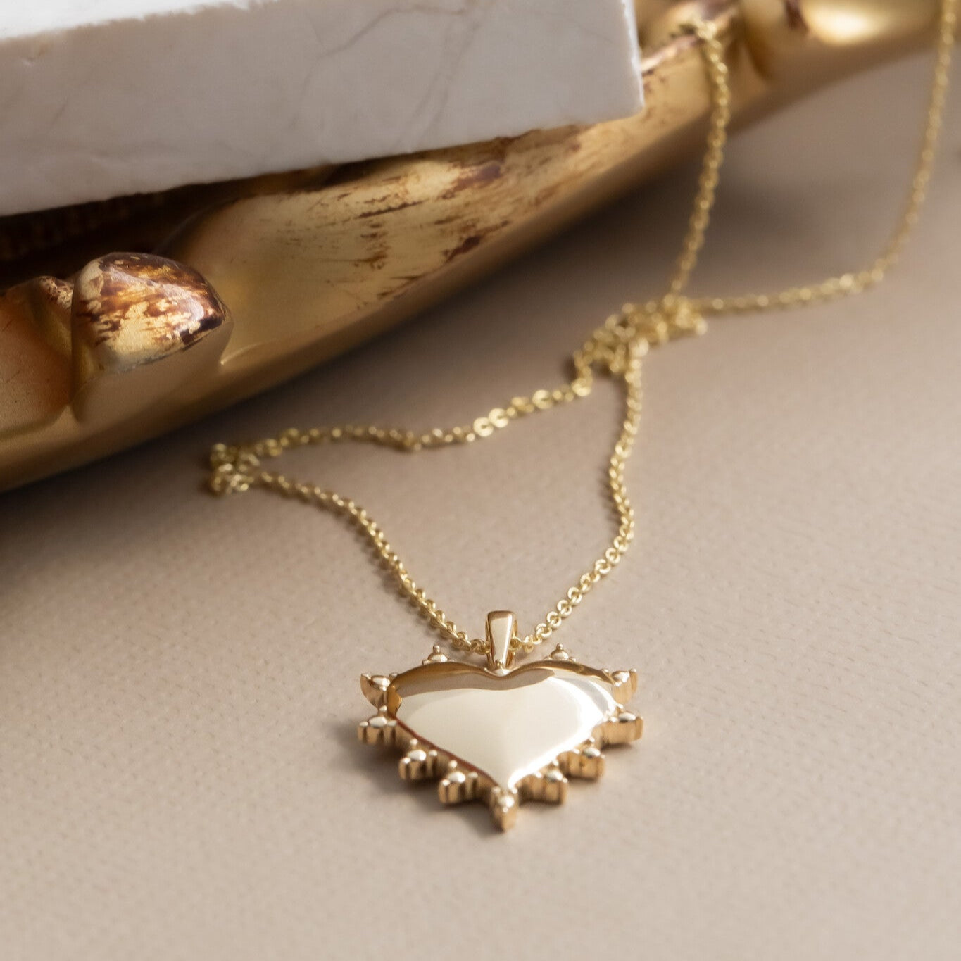 Gold necklace with a heart-shaped pendant on a neutral background