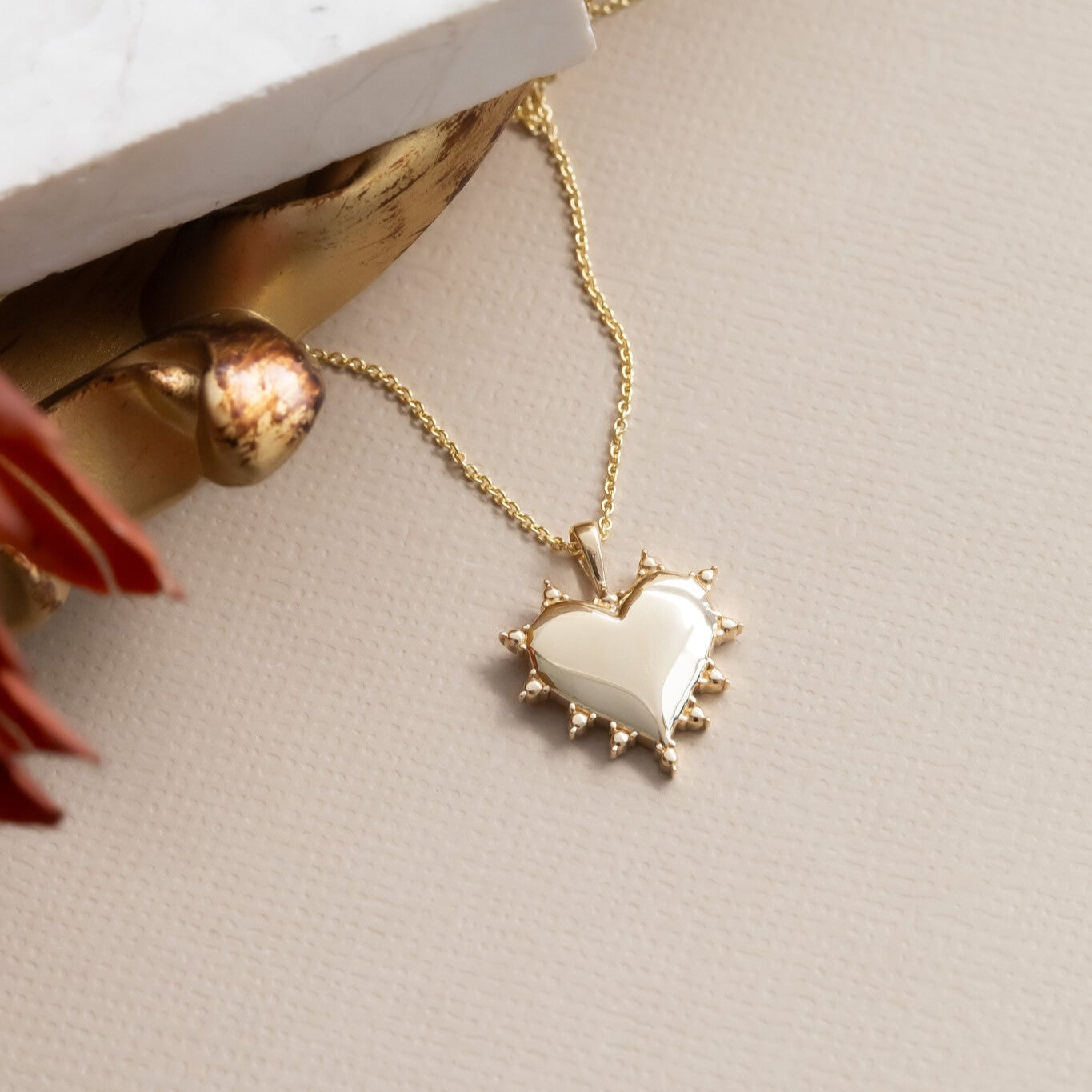 Gold necklace with a heart-shaped pendant on a neutral background