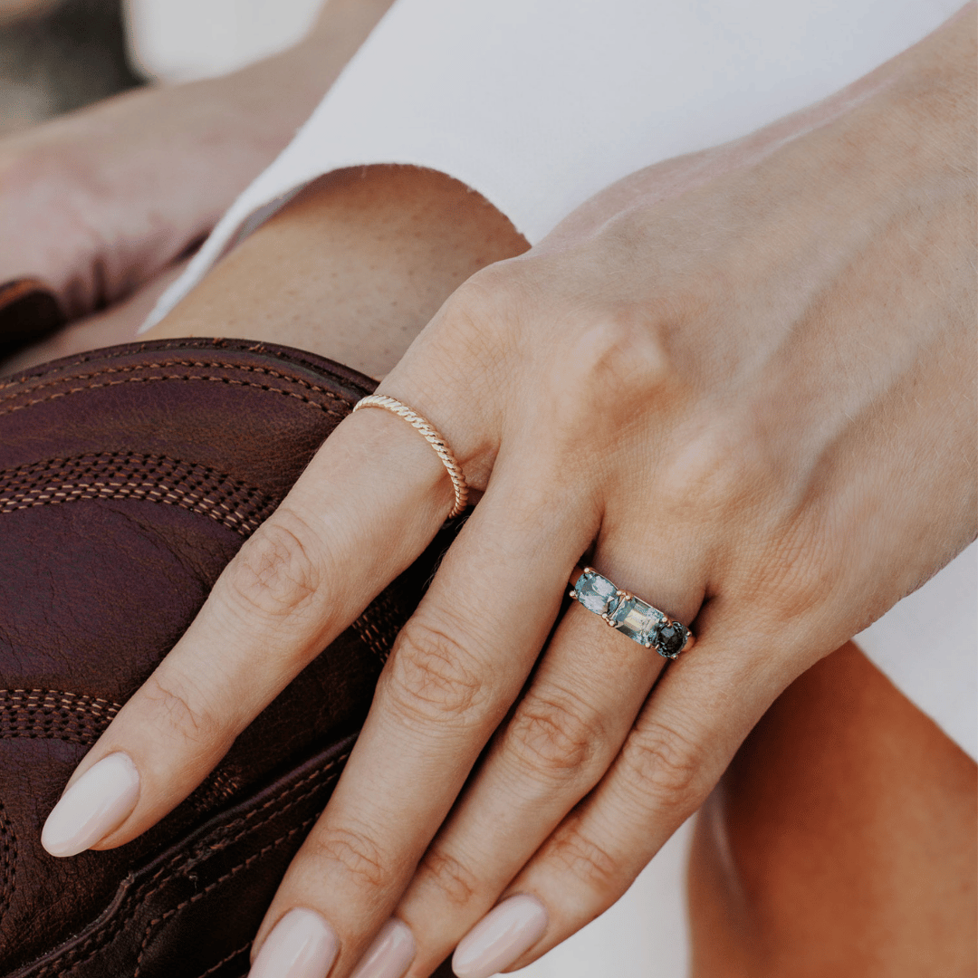 A 14k gold ring featuring three blue sapphire gemstones, displayed on the ring finger of a hand model. 