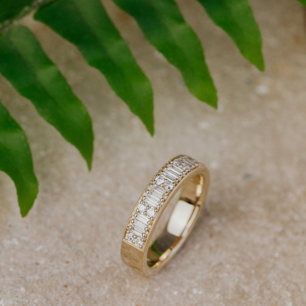 Gold band with diamonds on a textured surface with green leaves in the background