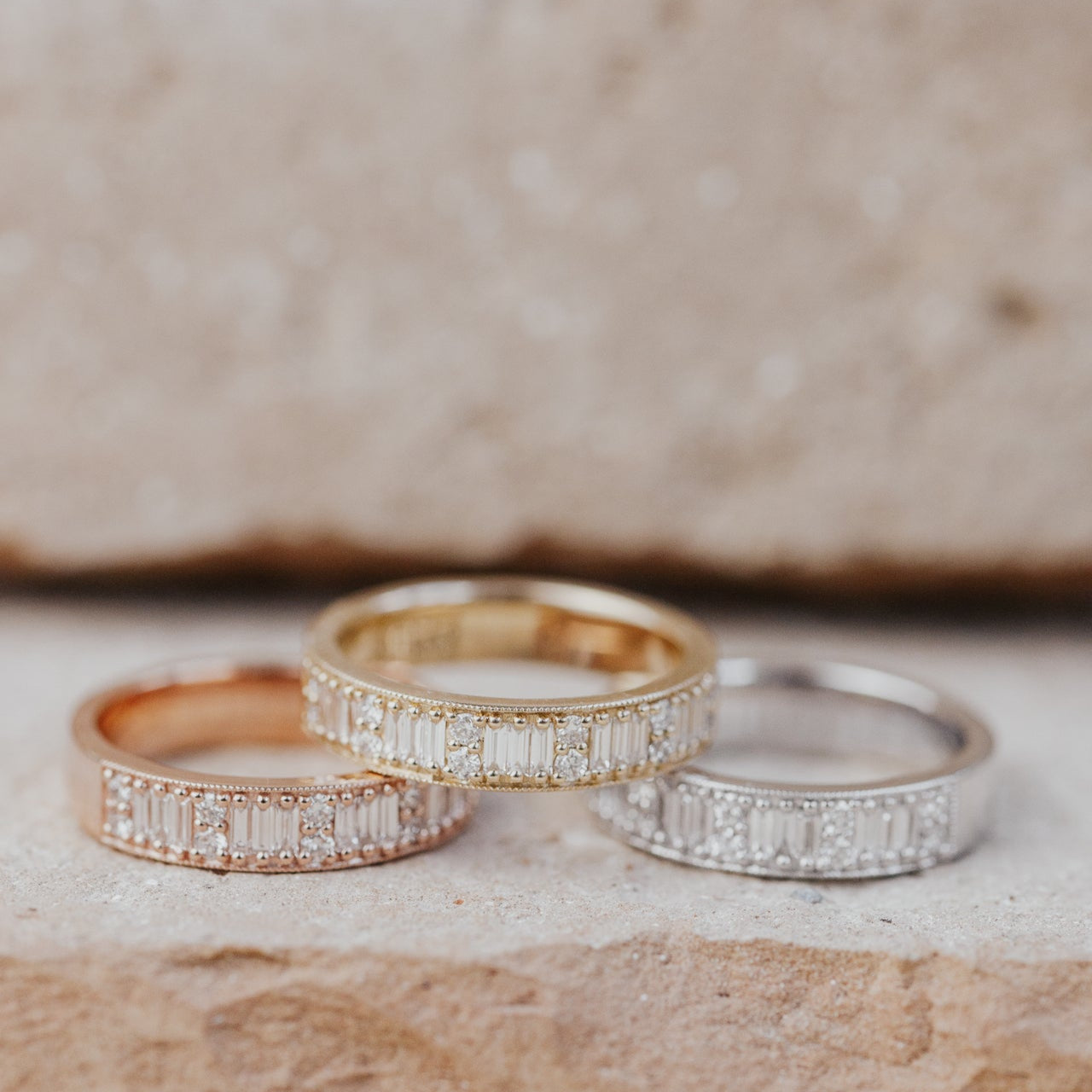 Three diamond bands in 14k yellow, white, and rose gold on a textured surface.