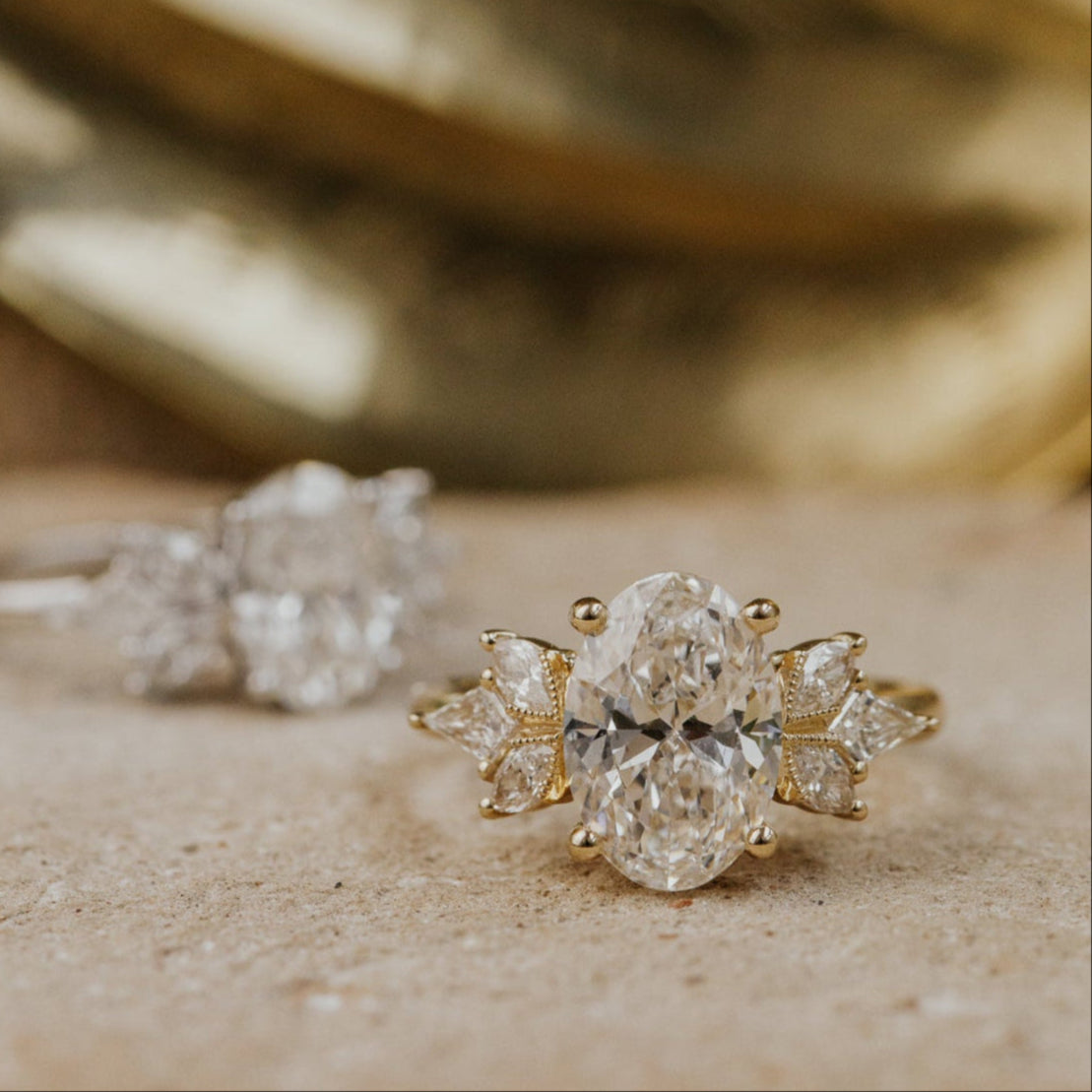 Gold oval  diamond earrings on a textured surface with a blurred gold background